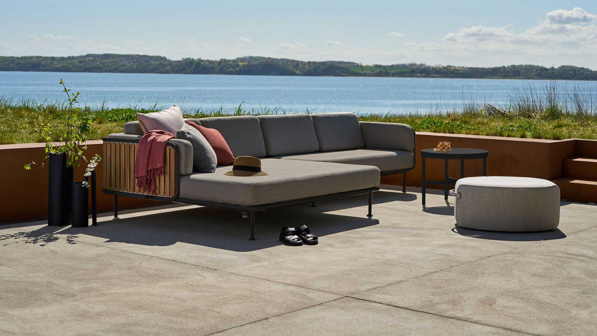 contemporary aluminum sectional with teak slats and grey cushions on a lakeside patio.