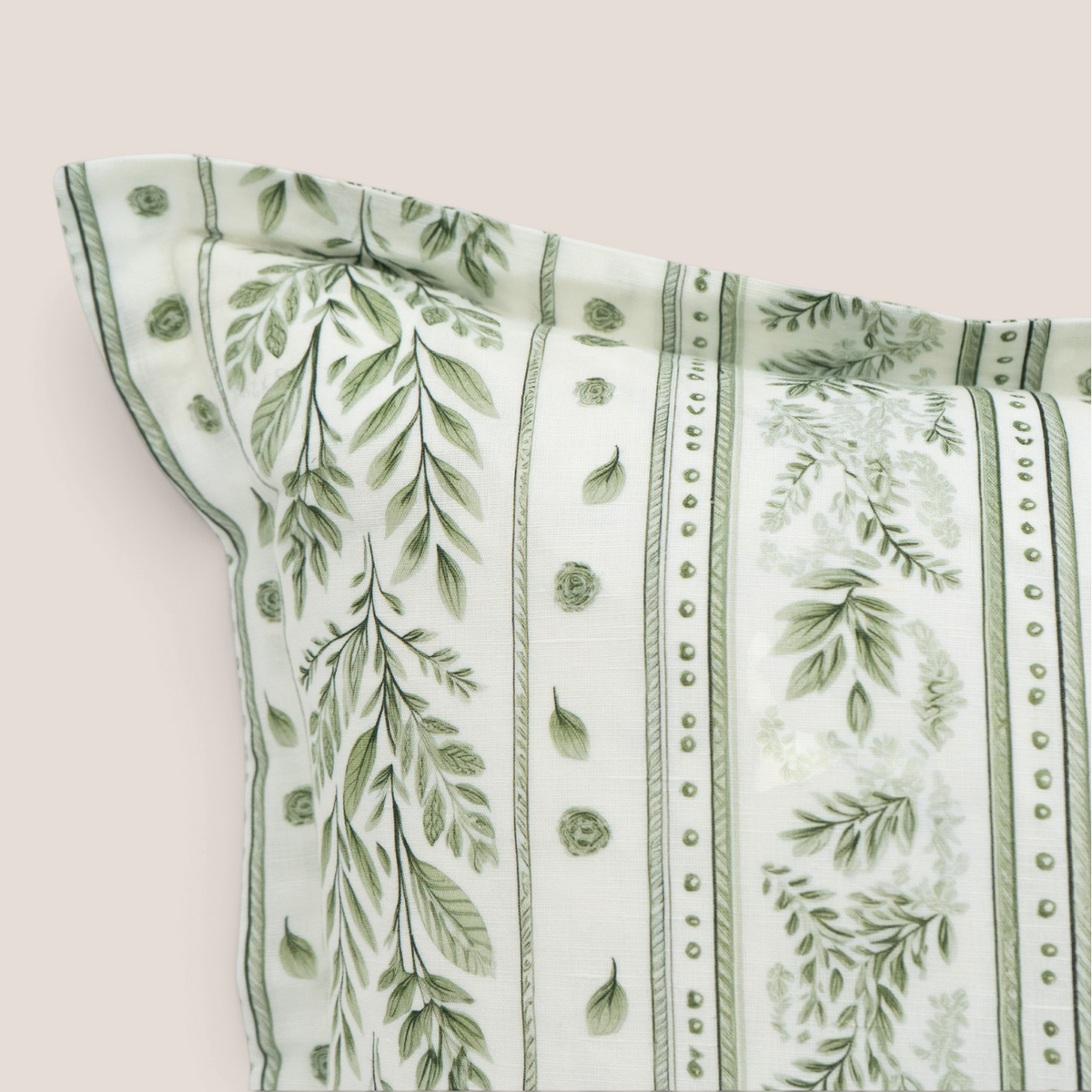 A close-up of a white fabric pillow, featuring a green botanical and leafy vine pattern with vertical stripes and dotted borders, set against a solid light beige background.