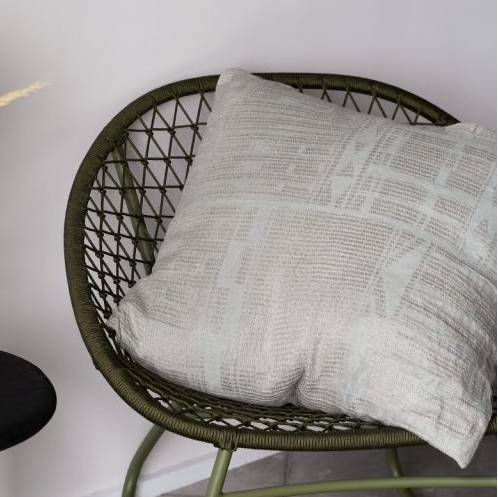 Wicker chair with a pillow next to a small table with a vase on a light gray floor.
