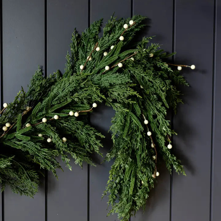 Green garland with white berries on a dark wooden door