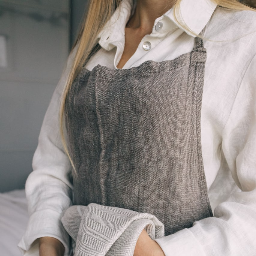 Person wearing a gray apron over a white shirt, holding a towel.