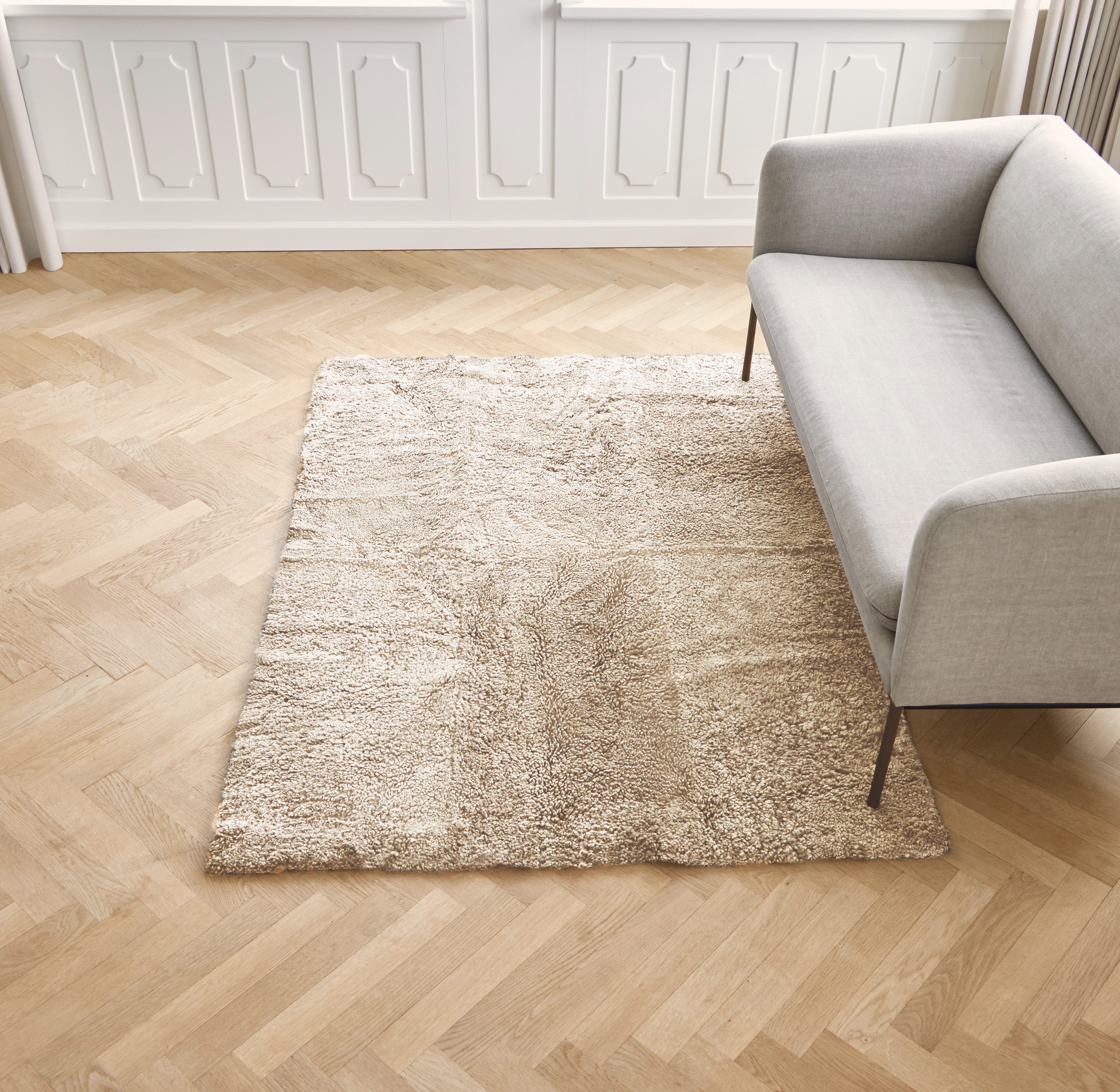 Beige sheepskin rug on a wooden floor with a gray sofa in a room.