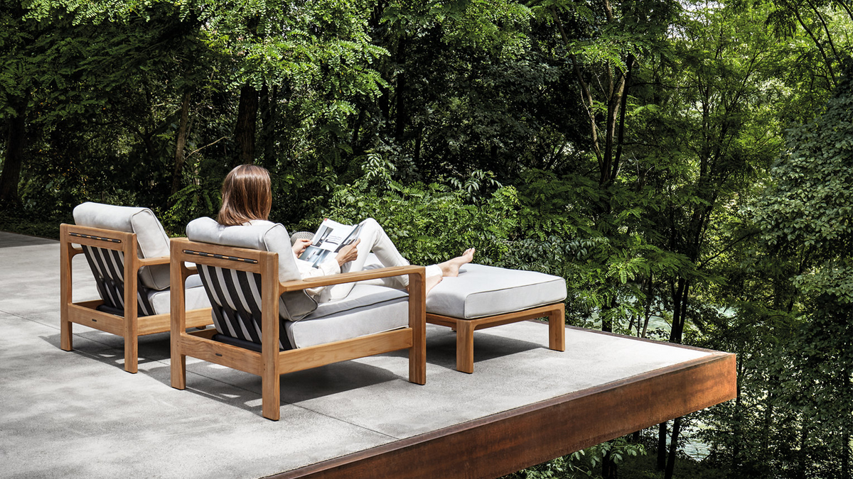 woman enjoying modern Gloster Loop lounge chair and ottoman on minimalist balcony overlooking forest