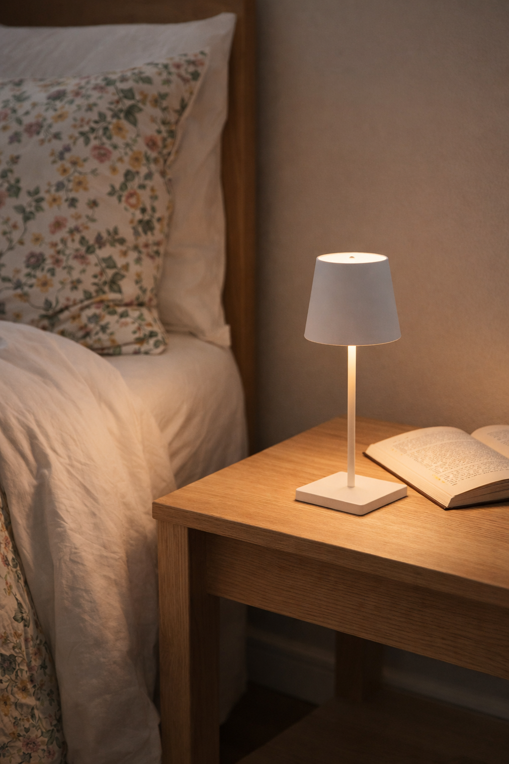 Small table lamp on a wooden nightstand next to a bed with floral pillows.