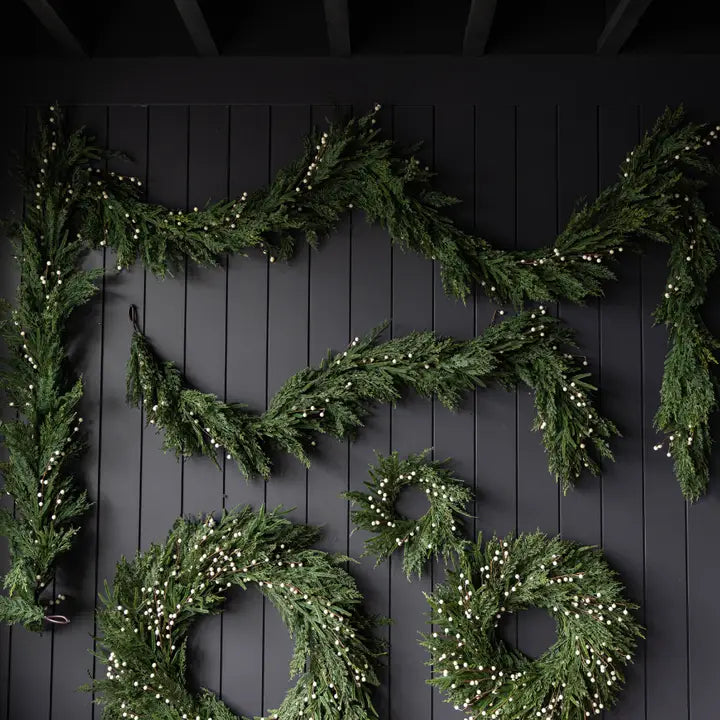 Decorative green garland and wreaths with white lights on a black wooden background