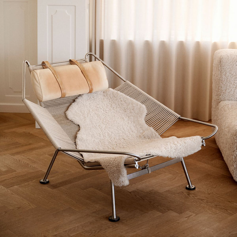 Modern lounge chair with sheepskin rug and cushions in a room with wooden floor and white curtains.