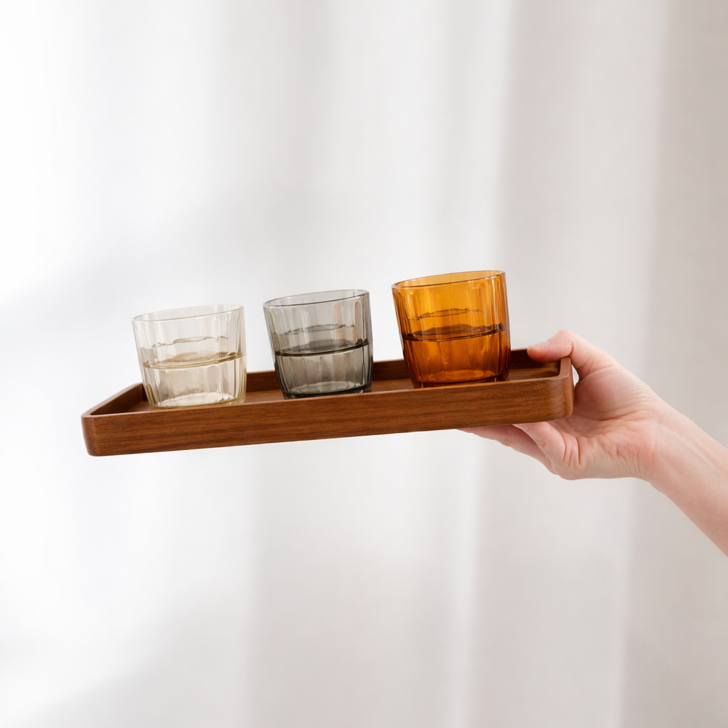 Hand holding a wooden tray with three colored glass cups against a white background
