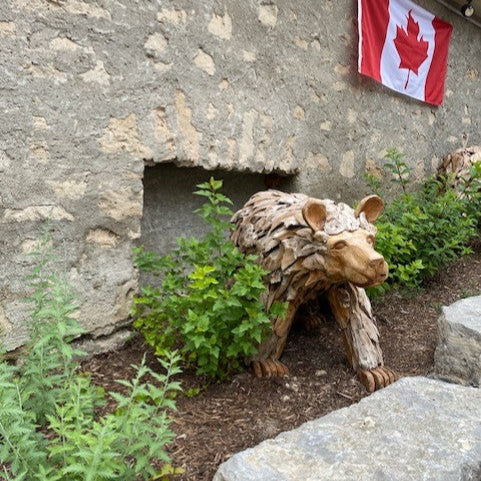 Wooden bear sculpture in front of a stone building with a Canadian flag.