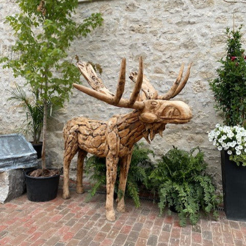 Wooden moose sculpture in front of a stone wall with plants around