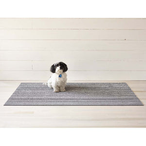Premium indoor and outdoor doormat, made from tufted, vinyl yarns and a vinyl backing.  Skinny striped pattern in dark and light grey colours.  A cute white and black puppy sits on the doormat.